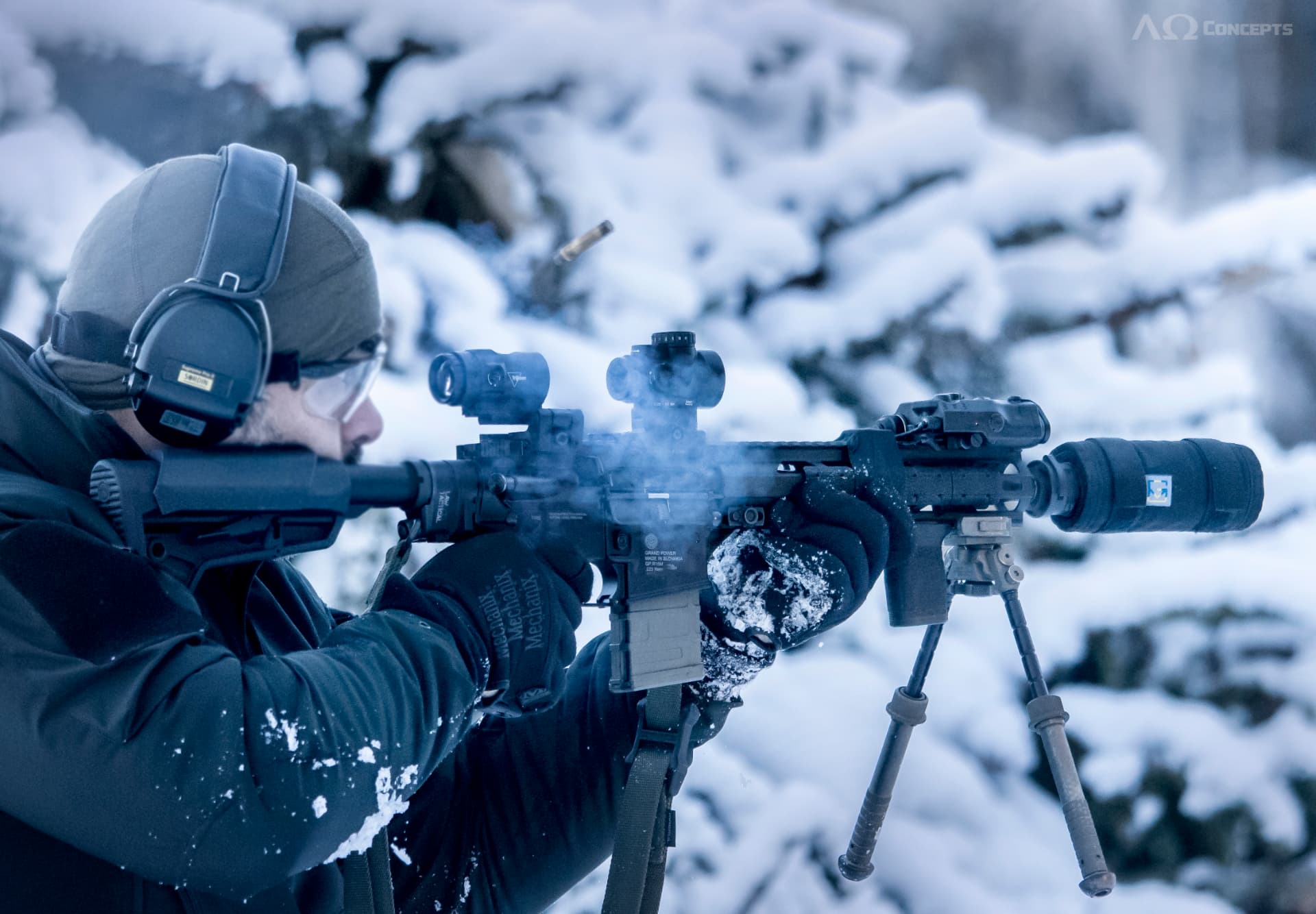 Shooter in winter gear firing a suppressed rifle in the snow